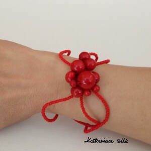 May include: Red beaded bracelet with a cluster of large red beads in the center. The bracelet is on a person's wrist.