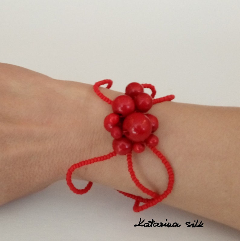 May include: Red beaded bracelet with a cluster of large red beads in the center. The bracelet is on a person's wrist.