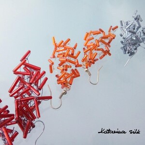 May include: Three pairs of dangle earrings made with small, rectangular beads. The earrings are in red, orange, and silver.