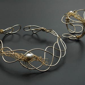 May include: A gold wire necklace and bracelet set with a single pearl accent. The necklace is a delicate, intricate design with a woven wire pattern. The bracelet is a simple, open circle design.