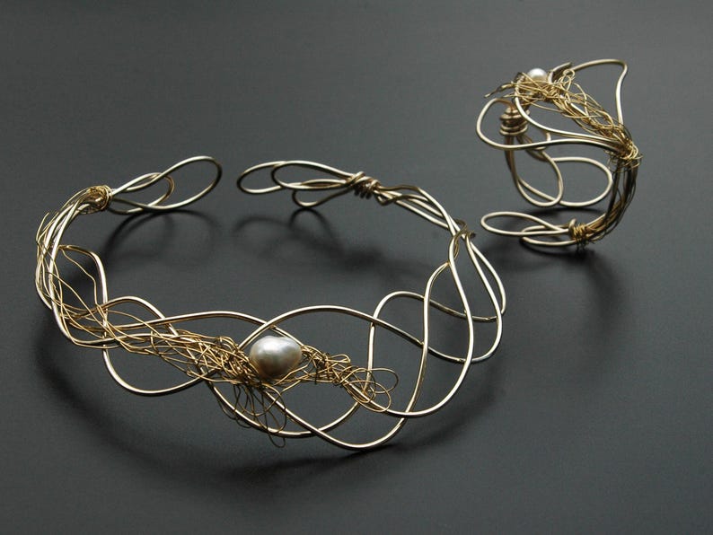 May include: A gold wire necklace and bracelet set with a single pearl accent. The necklace is a delicate, intricate design with a woven wire pattern. The bracelet is a simple, open circle design.
