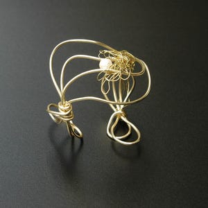 May include: A gold wire bracelet with a pearl accent. The wire is twisted and formed into a unique design.
