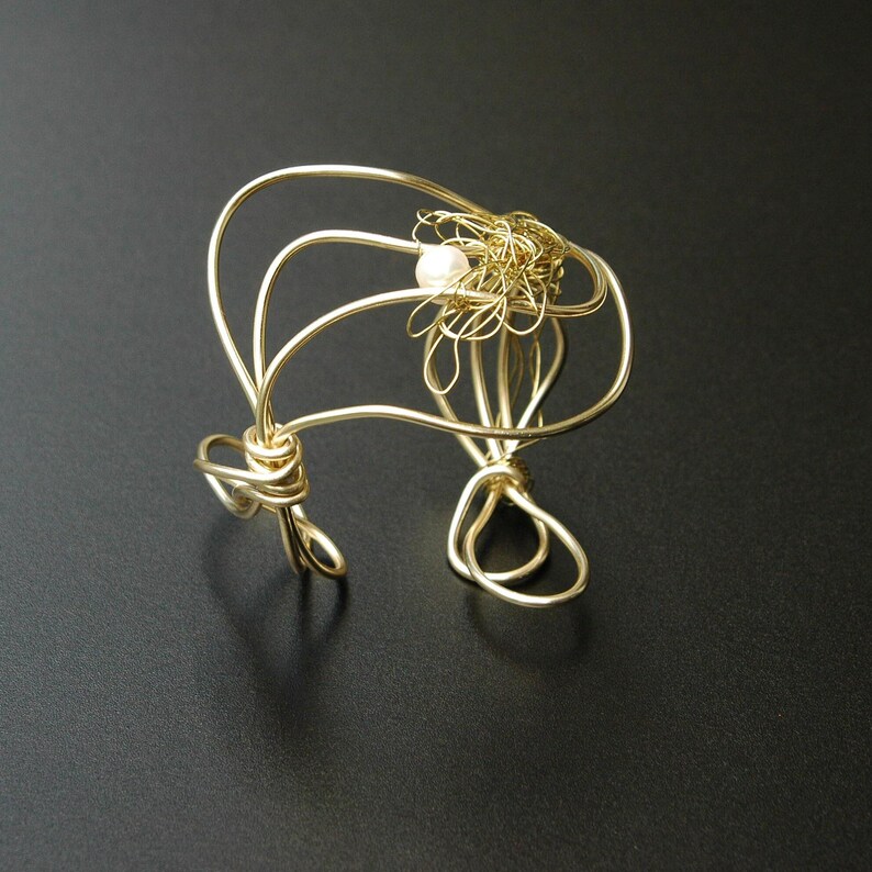 May include: A gold wire bracelet with a pearl accent. The wire is twisted and formed into a unique design.