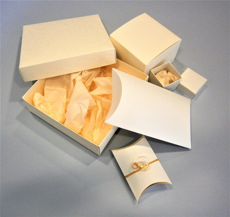 May include: A set of five white gift boxes, including a square box with a lid, a rectangular box with a lid, a pillow box, and two smaller square boxes. The boxes are made of sturdy cardboard and have a smooth, matte finish.