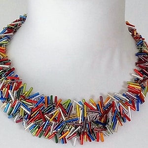 May include: A colorful necklace made of small, glass rods in various colors, including red, orange, yellow, green, blue, purple, and silver. The rods are arranged in a random pattern, creating a unique and eye-catching design.