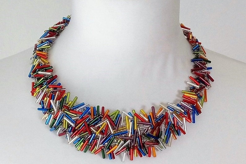 May include: A colorful necklace made of small, glass rods in various colors, including red, orange, yellow, green, blue, purple, and silver. The rods are arranged in a random pattern, creating a unique and eye-catching design.