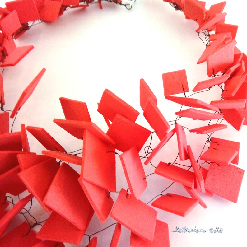 May include: A red necklace made of small squares connected by thin black wire. The squares are arranged in a cascading pattern, creating a unique and modern look.