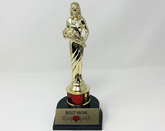 May include: Gold-colored trophy with a female figure holding a bouquet of flowers. The base is black with a red insert and a gold plaque that reads "BEST MOM" with a heart symbol.
