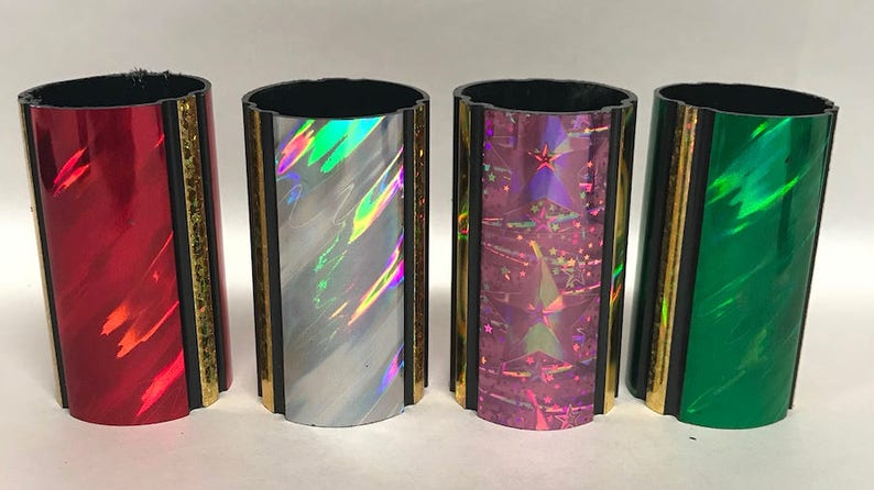 Może przedstawiać: Cztery ozdobne cylindry z iryzującymi wykończeniami. Cylindry są czarne z pozłacanymi obramowaniami i mają r&oacute;żne holograficzne wzory: czerwony, biały, r&oacute;żowy i zielony.