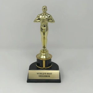May include: A gold-colored trophy with a male figure holding a star. The base is black with a gold trim and the words "WORLD'S BEST NEIGHBOR" are inscribed on a plaque.