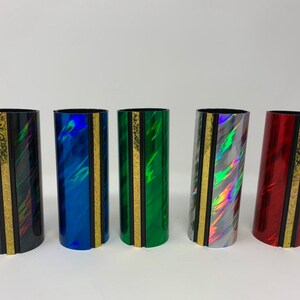 Może przedstawiać: Pięć kolorowych uchwyt&oacute;w na harmonijkę ustną z złotym paskiem i czarną obw&oacute;dką. Uchwyty są wykonane z błyszczącego, tęczowego materiału.