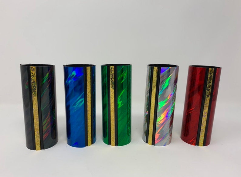 Może przedstawiać: Pięć kolorowych uchwyt&oacute;w na harmonijkę ustną z złotym paskiem i czarną obw&oacute;dką. Uchwyty są wykonane z błyszczącego, tęczowego materiału.