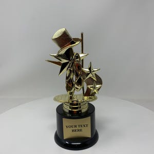May include: Gold-colored trophy with a top hat, stars, and ballet shoes. The base is black with a gold plate that says "YOUR TEXT HERE".