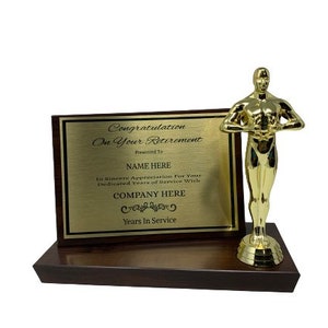 Può includere: Una statua premio dorata con una targa che recita "Congratulation On Your Retirement" e include spazio per un nome, un'azienda e gli anni di servizio.
