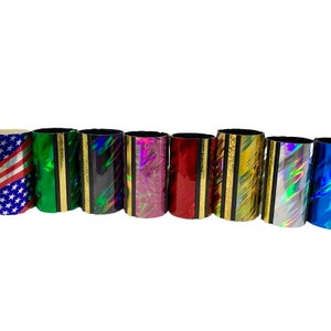 Może przedstawiać: Osiem kolorowych tub slide'&oacute;w do gitary. Slide'y są wykonane z metalu i mają r&oacute;żne holograficzne wzory. Slide'y są ułożone w rzędzie od lewej do prawej.