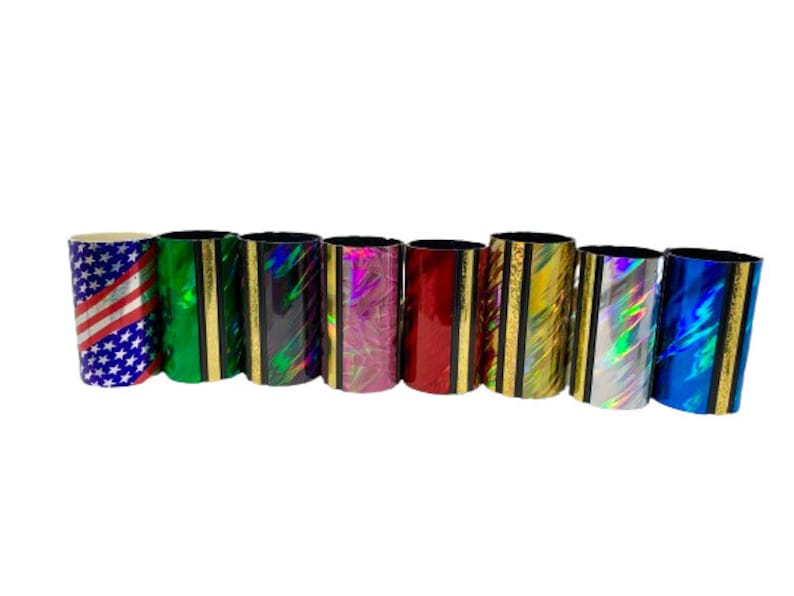 Może przedstawiać: Osiem kolorowych tub slide'&oacute;w do gitary. Slide'y są wykonane z metalu i mają r&oacute;żne holograficzne wzory. Slide'y są ułożone w rzędzie od lewej do prawej.