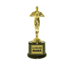 May include: A gold-colored trophy with a figure of a person holding a trophy. The base of the trophy is black and has a gold plaque with the text "LA MEJOR MAMÁ" on it.