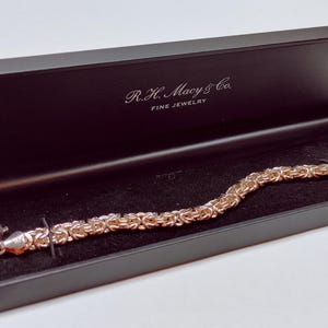 May include: A rose gold Byzantine chain bracelet rests inside a black jewelry box. The box is open, revealing a dark velvet interior. The bracelet is secured with a lobster clasp. The box is labeled "R.H. Macy & Co. FINE JEWELRY."