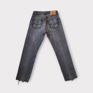 May include: Faded black denim jeans with a distressed look. The jeans have a classic five-pocket design, a leather patch, and a red tag. The bottom hems are frayed. The jeans are displayed on a white background.