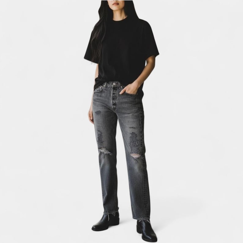 May include: A person wearing a black crew neck t-shirt and distressed gray jeans with ripped knees. The person is also wearing black ankle boots. The outfit is casual and modern.