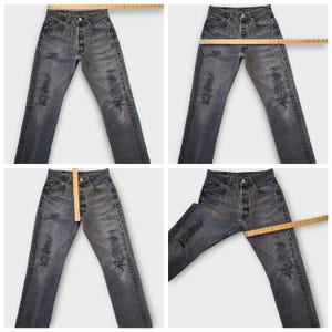 May include: Faded black denim jeans with distressed details. The jeans have a button fly and multiple pockets. Measurements are shown with a wooden ruler. The jeans are a classic style.