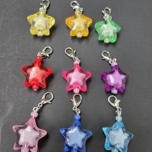 May include: Nine star-shaped charms in various colors, including yellow, orange, green, red, pink, purple, light blue, and dark blue. Each charm has a silver-colored clasp and a small bead. The charms are made of translucent plastic.