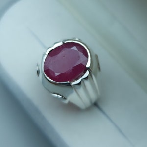 Könnte beinhalten: Ein silberner Ring mit einem großen, oval geschliffenen Rubin. Der Rubin hat eine tiefe, satte rote Farbe und ist in einem polierten Silberband gefasst. Der Ring hat ein klassisches, elegantes Design.