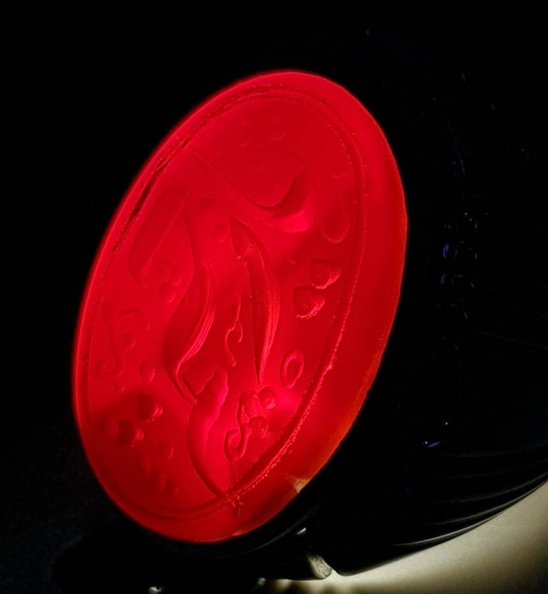 May include: A red oval-shaped wax seal with a decorative design. The seal is made of red wax and has a raised design.