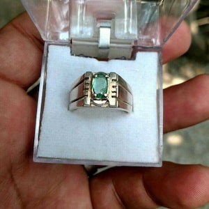May include: A silver ring with a green oval gemstone set in the center. The ring has a simple design with a band that is slightly wider than the setting.