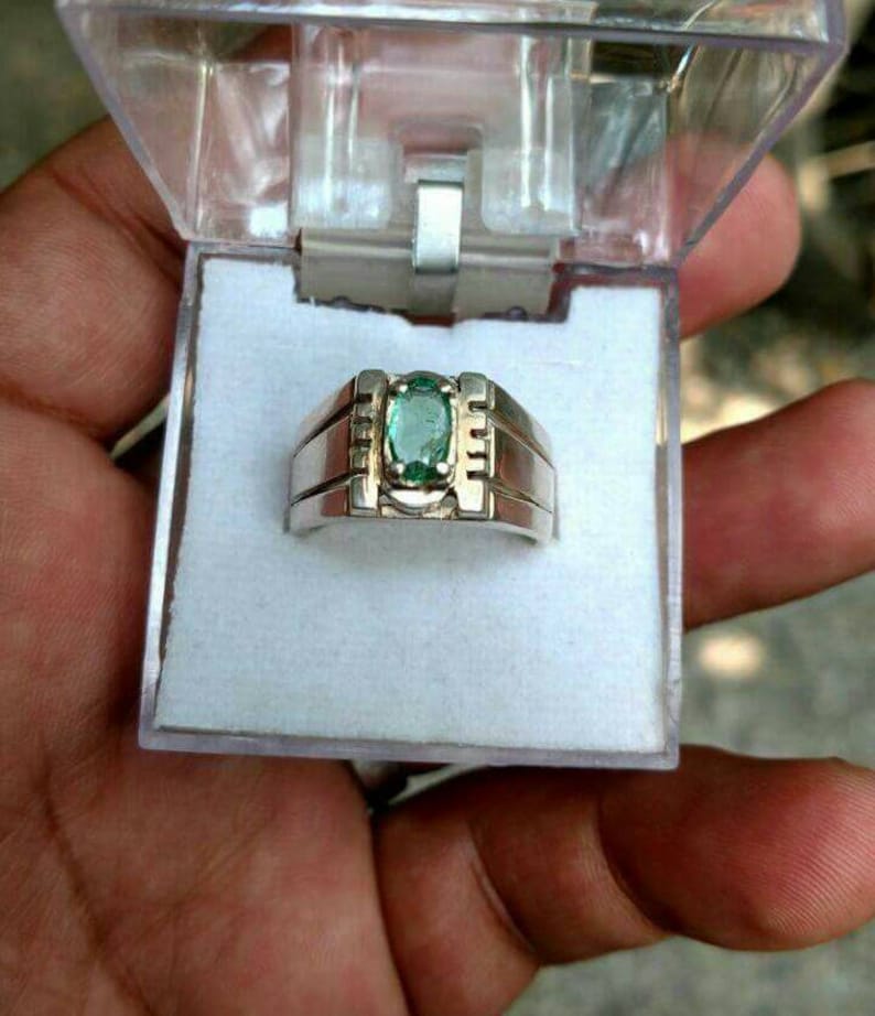 May include: A silver ring with a green oval gemstone set in the center. The ring has a simple design with a band that is slightly wider than the setting.