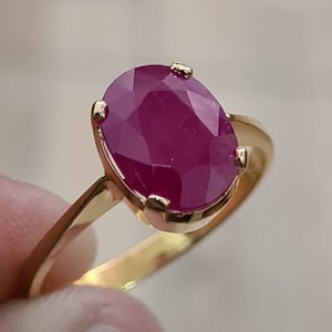 May include: A gold ring with a large, oval-shaped ruby gemstone. The ruby is a deep red color and has a faceted cut.