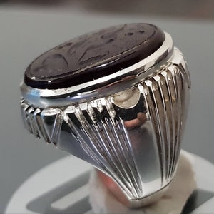 May include: A silver ring with a dark red oval gemstone. The ring has a detailed design on the band.