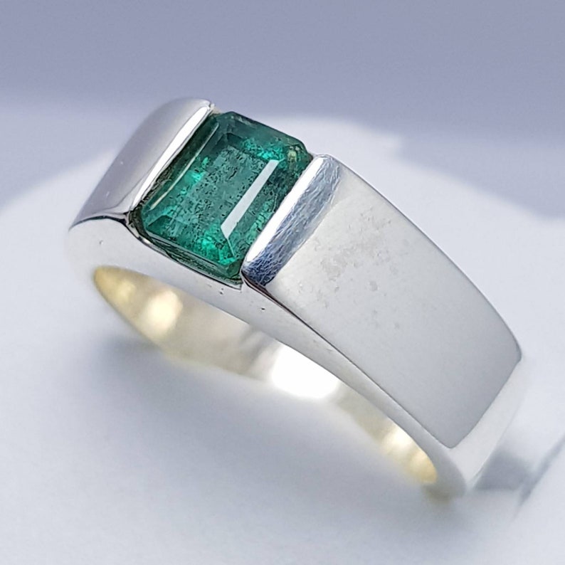 May include: A silver ring with a green emerald gemstone set in a square shape.