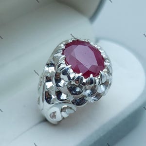Peut inclure: Une bague en argent avec un design orné mettant en vedette une grande pierre précieuse de rubis rouge de forme ovale.