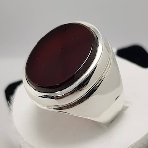 May include: A silver ring with a dark red oval gemstone set in a bezel setting.