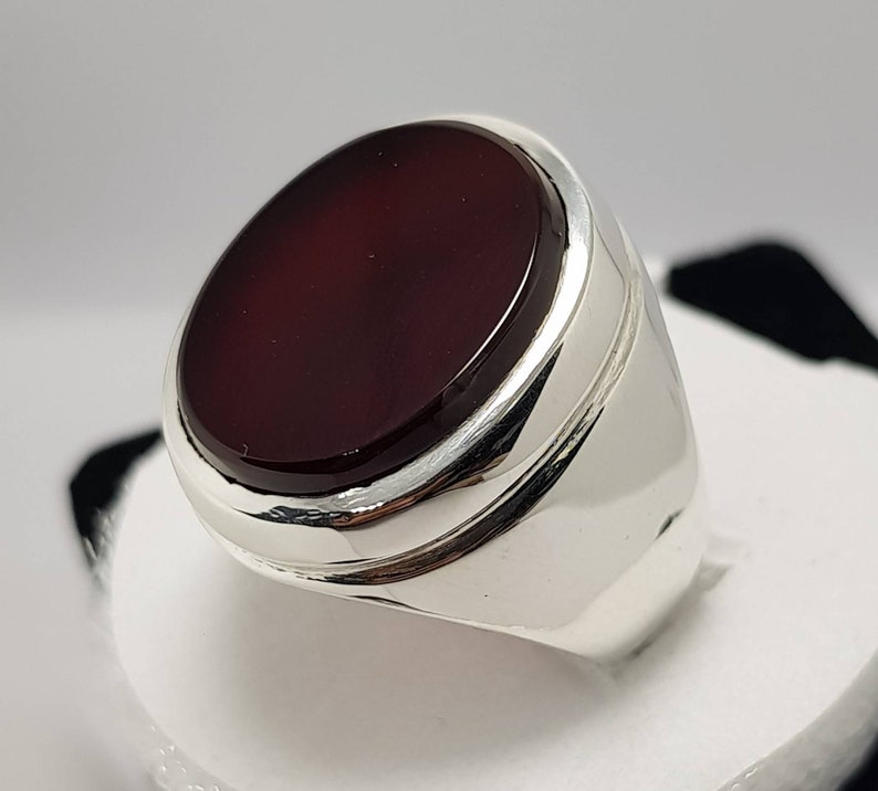 May include: A silver ring with a dark red oval gemstone set in a bezel setting.