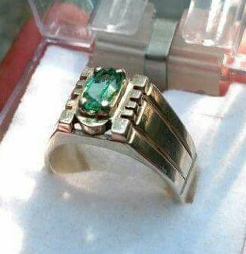 May include: A silver ring with a green emerald gemstone set in a rectangular shape. The ring has a textured band with a stepped design.