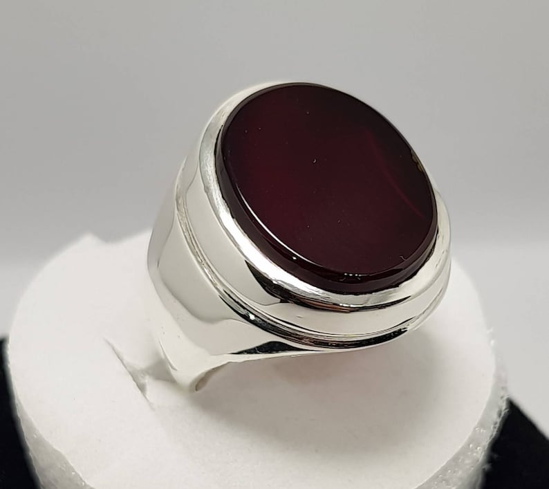 May include: A silver ring with a large, oval-shaped, dark red gemstone set in a silver bezel.