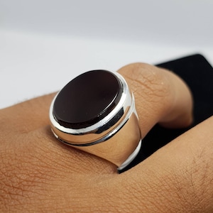May include: A silver ring with a dark red oval gemstone. The ring has a polished silver band with a raised edge around the gemstone.