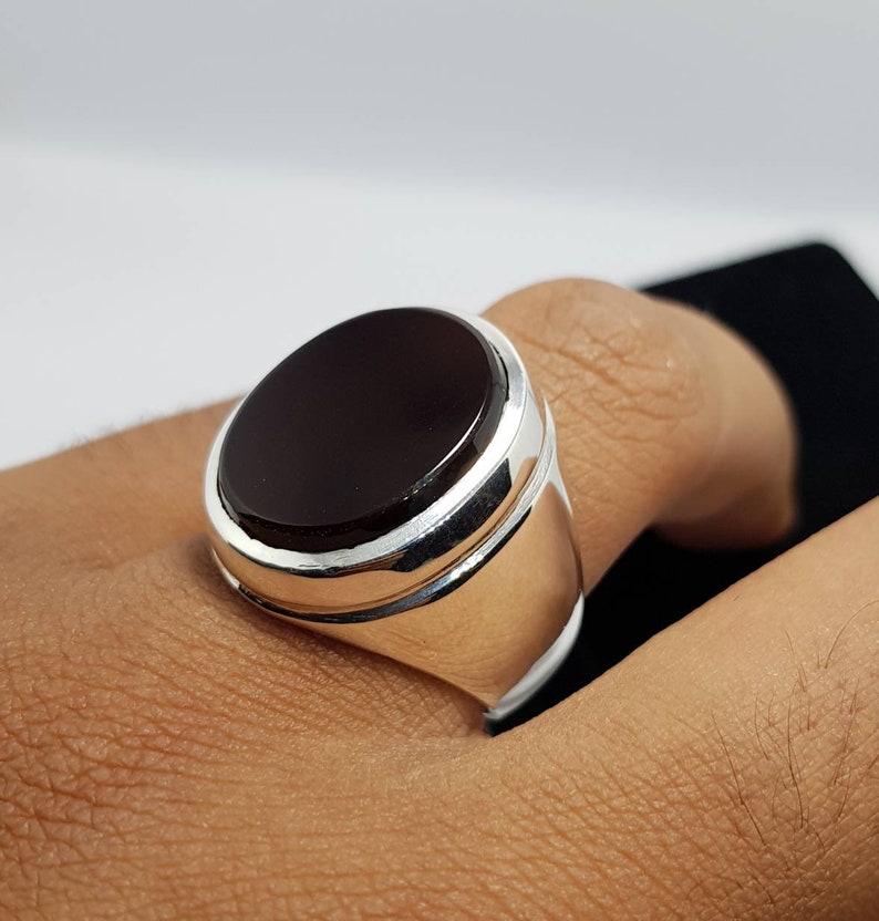 May include: A silver ring with a dark red oval gemstone. The ring has a polished silver band with a raised edge around the gemstone.