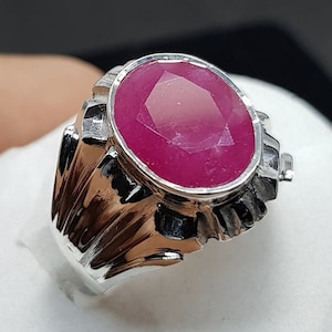 Könnte beinhalten: Ein silberner Ring mit einem großen, ovalen, rosafarbenen Rubin, der in einer detaillierten, verzierten Fassung sitzt.