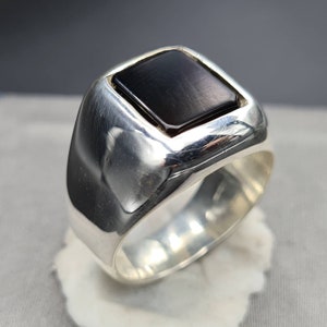 May include: A silver ring with a square black gemstone set in a raised bezel.