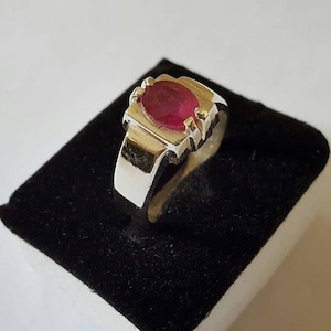 Op de afbeelding: Een zilveren ring met een rode ovale edelsteen in een kraalbezetting.