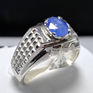 May include: A silver ring featuring a blue oval gemstone set in a prong setting. The band of the ring has a textured design.
