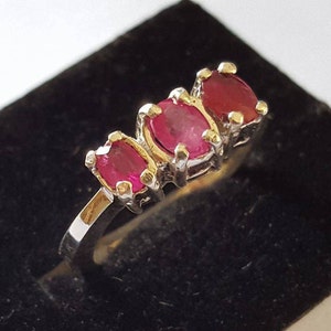 May include: A silver ring with three oval-shaped ruby gemstones set in a row.