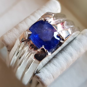 May include: A silver ring featuring a deep blue sapphire gemstone. The ring has a textured band with multiple ridges.