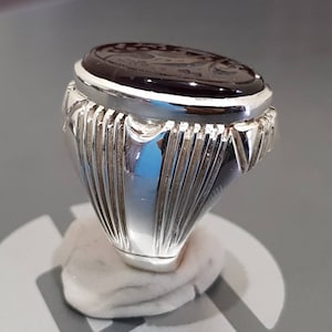 May include: A silver ring with a dark brown oval gemstone. The ring has a detailed, textured band.