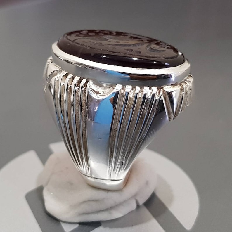 May include: A silver ring with a dark brown oval gemstone. The ring has a detailed, textured band.