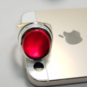 May include: A silver ring with a large, oval-shaped, red gemstone.