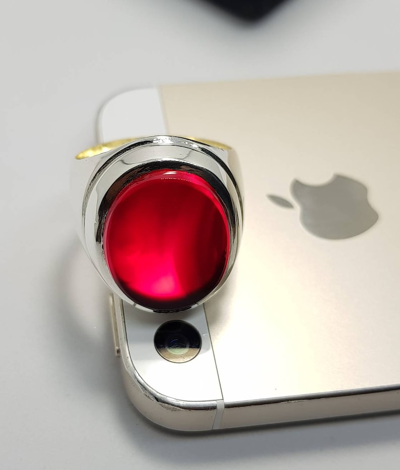 May include: A silver ring with a large, oval-shaped, red gemstone.
